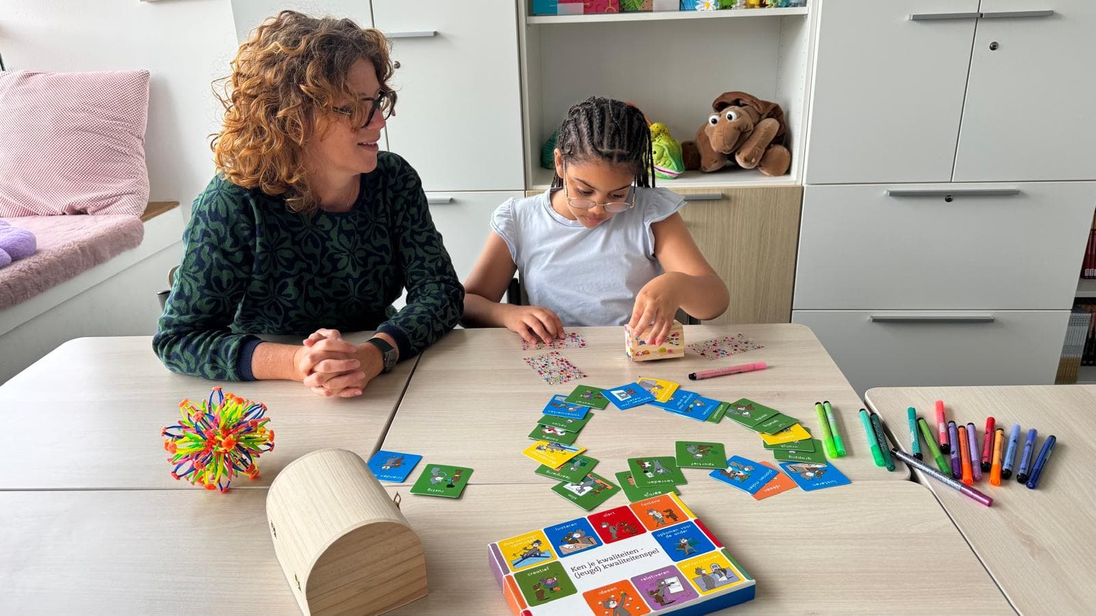 Moeder en kind aan tafel met het kwaliteitenspel en het houten schatkistje